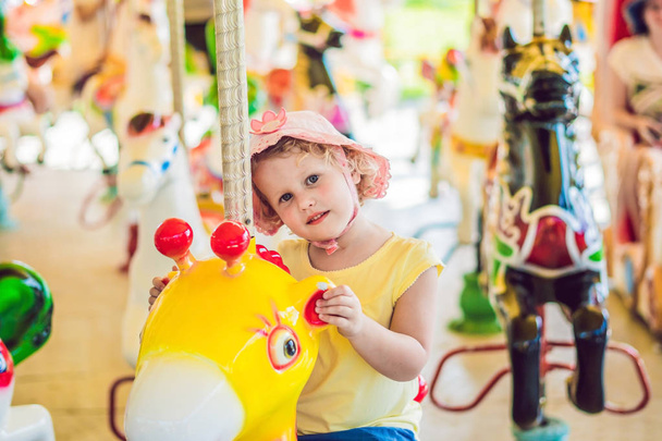 Cute little girl enjoying in funfair and riding on colorful carousel house - 写真・画像