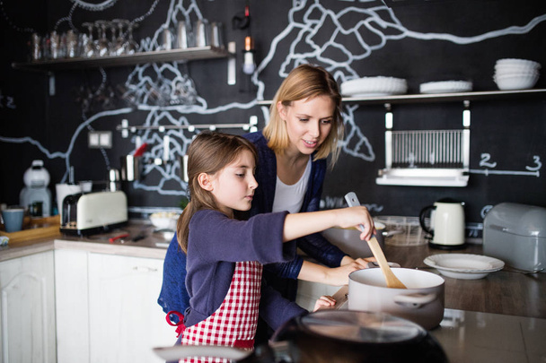 A small girl with her mother cooking at home. - Photo, Image
