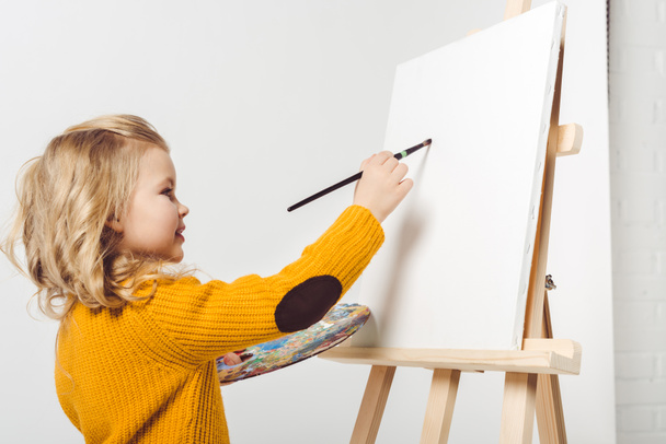 glückliches kleines Kind Malerei auf Leinwand mit Ölfarbe auf Weiß - Foto, Bild