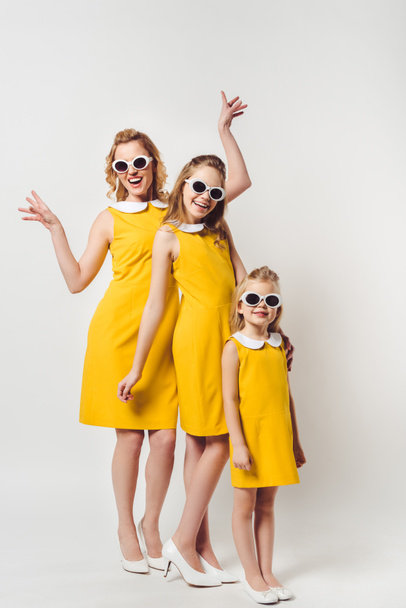 happy mother and daughters in similar retro style yellow dresses on white - Foto, Bild