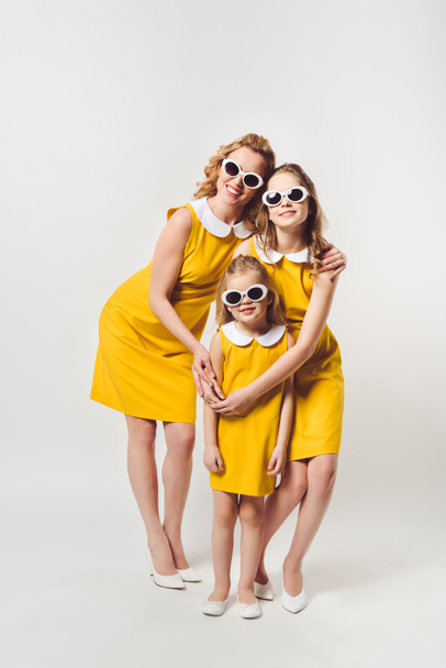 embracing mother and daughters in similar retro style yellow dresses on white - Valokuva, kuva