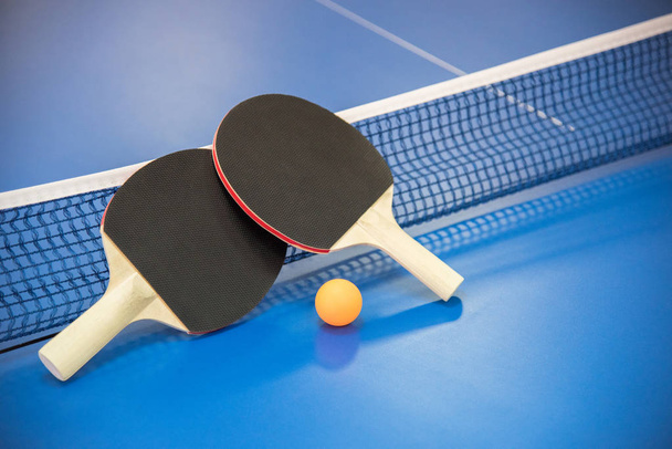 Оранжевый мяч для настольного тенниса и две ракетки красного и черного ко
 - Фото, изображение