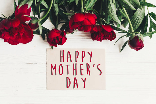 幸せな母の日テキスト署名クラフト紙カードに白い木製の素朴な背景、フラットで美しい赤い牡丹が横たわっていた。モダンなグリーティング カード。母の日。スタイリッシュな花が咲く - 写真・画像