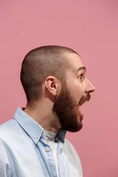 The young emotional surprising man screaming on pink studio background - 写真・画像