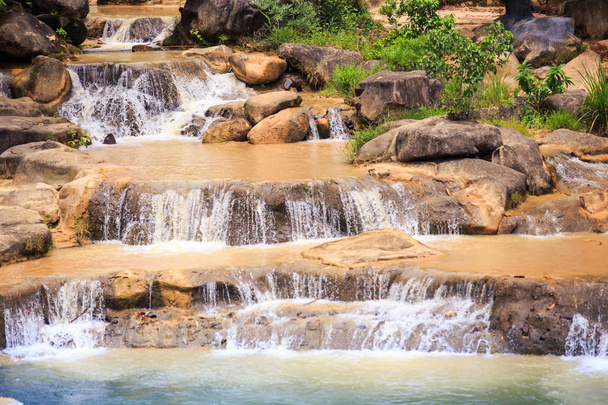 cascade of small foamy mountain river waterfalls along brownstones in tropical park - Photo, Image
