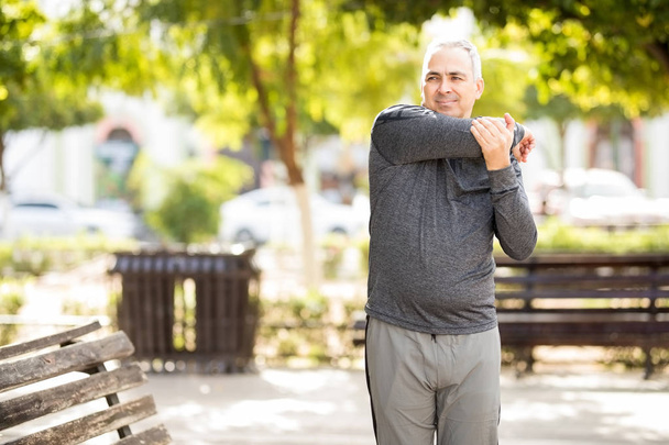 Feliz hombre maduro estirando los brazos antes de hacer ejercicio en el parque
 - Foto, imagen