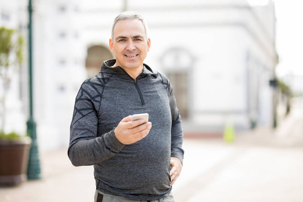 Good looking middle-aged man with a mobile phone after morning run in the city - Photo, Image