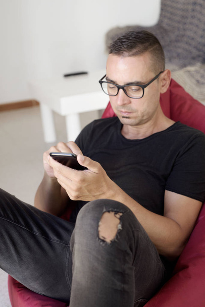 man using his smartphone sitting in bean bag chair - Photo, Image