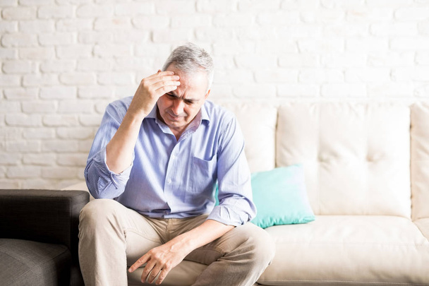 Spaanse man van middelbare leeftijd raken zijn voorhoofd en een hoofd pijn thuis - Foto, afbeelding
