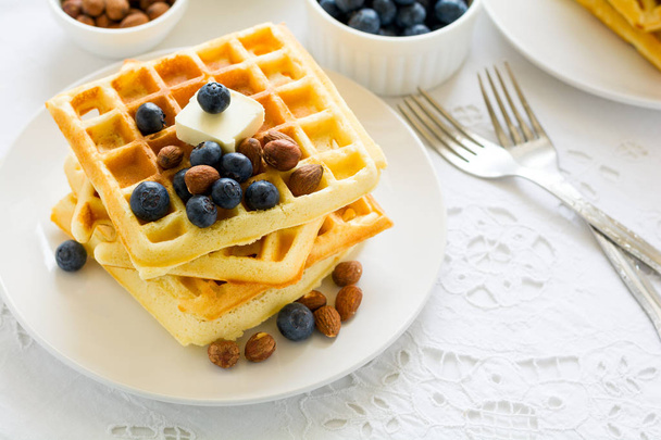 Healthy breakfast. Belgian waffles with butter, blueberry and nuts on white tablecloth. Selective focus - 写真・画像