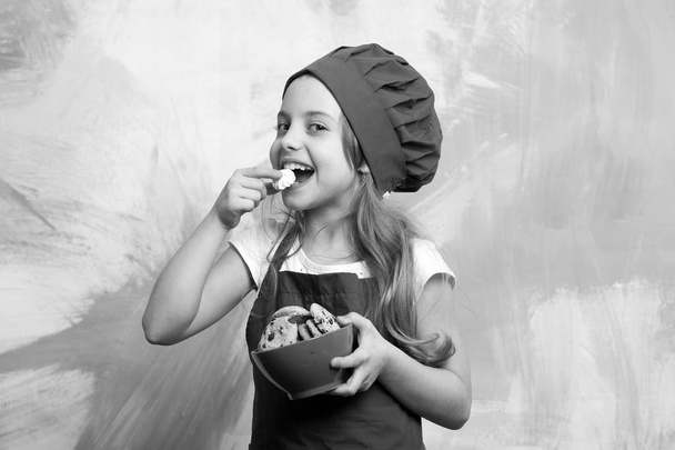 happy small girl eating chocolate cookies dessert in cook hat - Valokuva, kuva