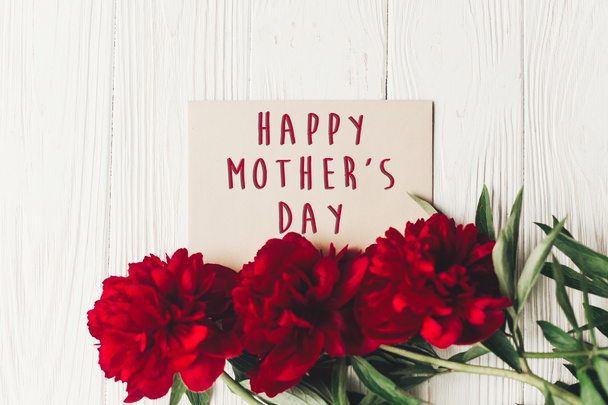 happy mother's day text sign on craft paper card beautiful red peonies on white wooden rustic background, flat lay. modern greeting card. mothers day. stylish blooming flowers - Foto, imagen