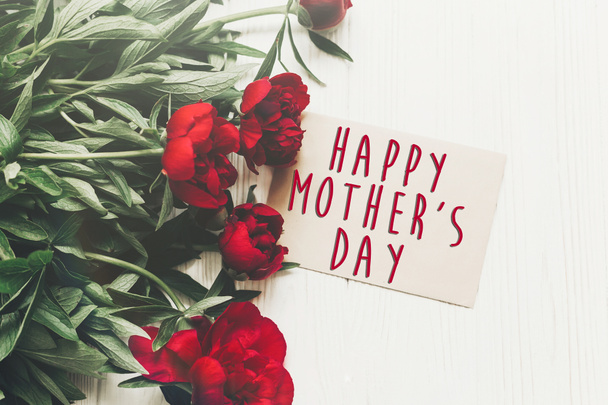 Happy mother's day tekst Zaloguj się na karcie papieru rzemiosła leżał piękny czerwony piwonie na białe drewniane tła rustykalne, płaskie. nowoczesne karty z pozdrowieniami. dzień matki. stylowe kwitnących kwiatów - Zdjęcie, obraz