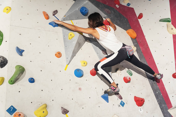Woman practicing rock climbing on artificial wall indoors. Active lifestyle and bouldering concept. - Photo, image