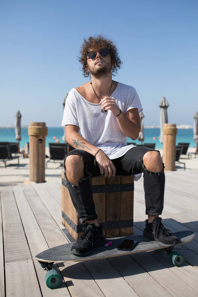 Stylish man sitting near the beach and smoking. - Fotoğraf, Görsel