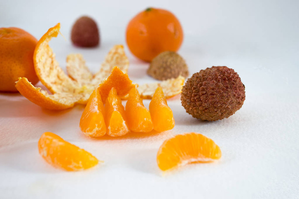 Mandarinen auf weißem Hintergrund mit Lobuli, Schale, Zitrone und Litschi. Seitenansicht, schließen. Citrus reticulata. litchi chinensis. - Foto, Bild