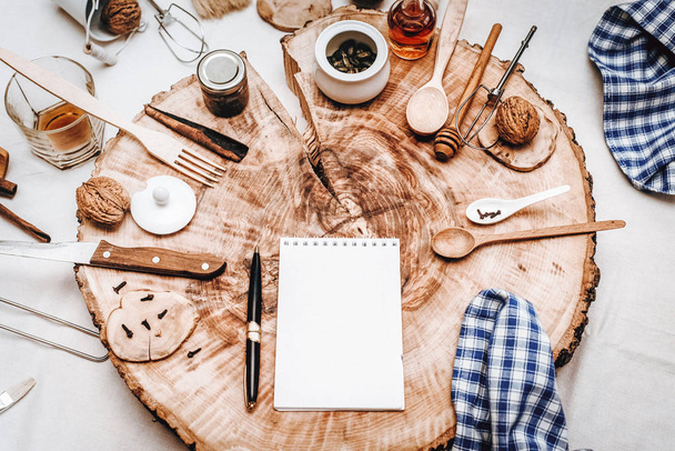 Vista superior de madeira serrada com notebook, caneta e diferentes acessórios de cozinha no fundo
 - Foto, Imagem