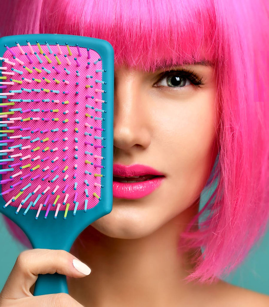 Closeup portrait of happy fashion brunette woman close mouth with colorful pink blue yellow small hair comb brush in pink wig - Photo, Image