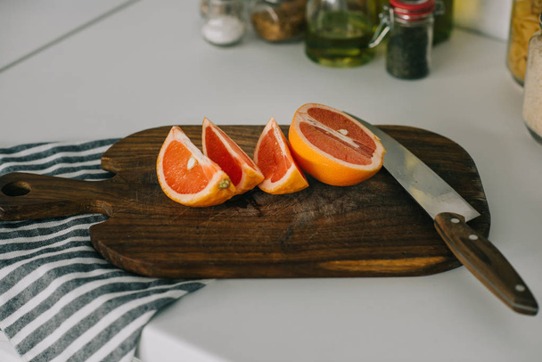 cut grapefruit with knife on wooden board in kitchen - Photo, Image