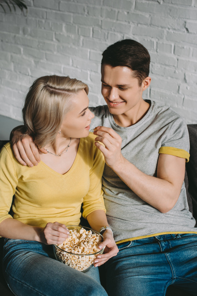 boyfriend feeding girlfriend with popcorn on sofa - Foto, imagen