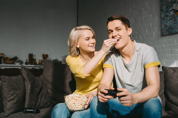 smiling girlfriend feeding boyfriend with popcorn at home - Fotografie, Obrázek