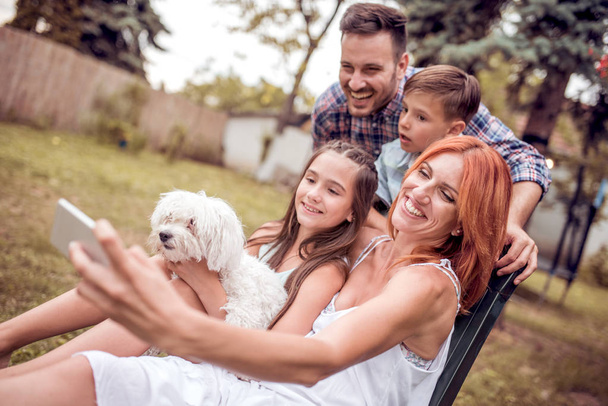 Familia feliz con perro tomando selfie con teléfono inteligente en el park.Family, mascota, tecnología y concepto de personas
. - Foto, Imagen