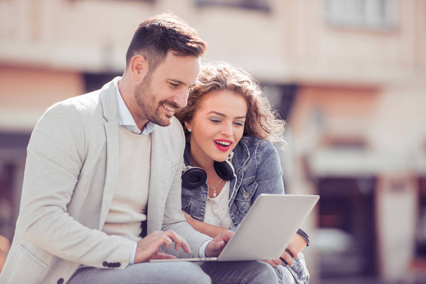 Young couple using a laptop outdoors and looking happy. - Photo, Image