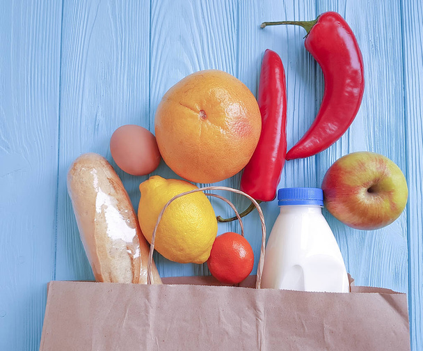 paper bag with different useful food, vegetables and fruits on blue wooden - Photo, Image