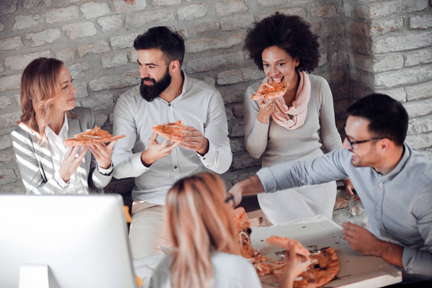 Szczęśliwy młody biznes drużyna jedzenie pizzy w biurze. Koncepcja biznes, jedzenie i osób. - Zdjęcie, obraz