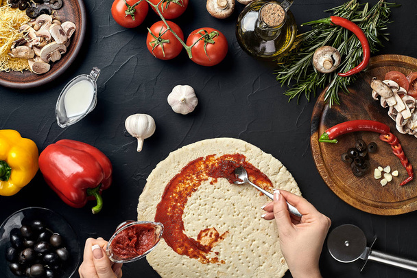 Manos de panadero agregando ingredientes a la pizza durante la preparación de la pizza en la cocina
 - Foto, imagen