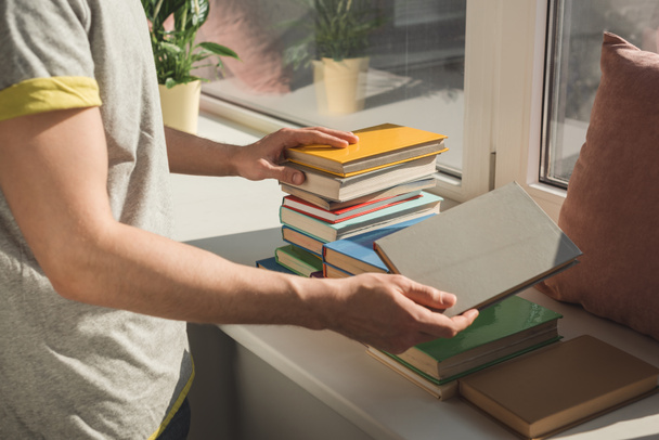 cropped image of man holding books at windowsill - Foto, Imagem