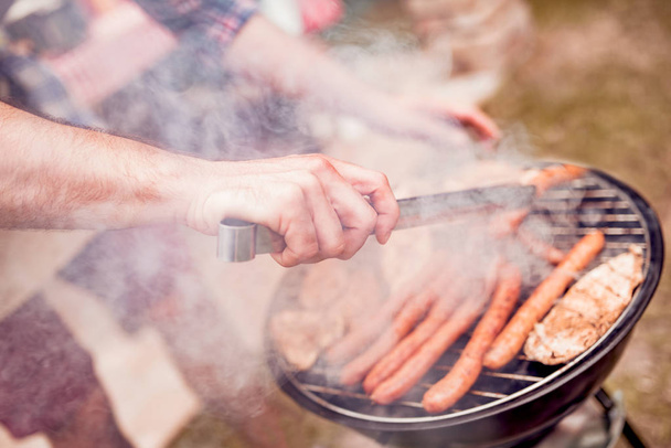 夏の楽しみ。家の裏庭で夏の家族の夕食のバーベキューで肉を料理人. - 写真・画像