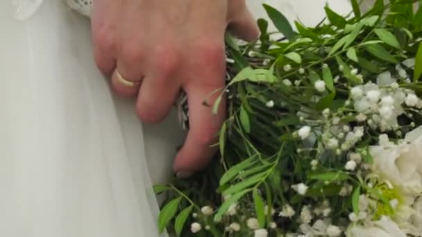 Pěkné svatební kytice v ruce nevěsty. Klip. Snoubenka v krásných bílých šatech drží krásné Kytice svatební květiny vyrobené z nabídky růží v ruce - Záběry, video