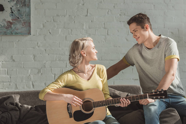 namorada tocando guitarra acústica e olhando para o namorado em casa
 - Foto, Imagem