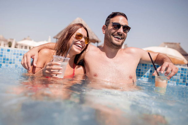 Portrait d'un beau jeune couple souriant et buvant un cocktail dans une piscine
. - Photo, image