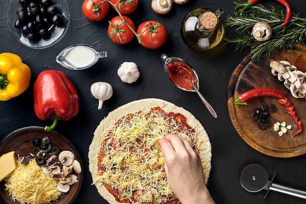 Hände des Bäckers fügen Zutaten während der Pizzazubereitung in der Küche in die Pizza ein - Foto, Bild