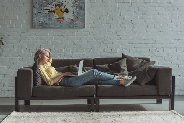 side view of beautiful girl lying with laptop on sofa - Photo, Image