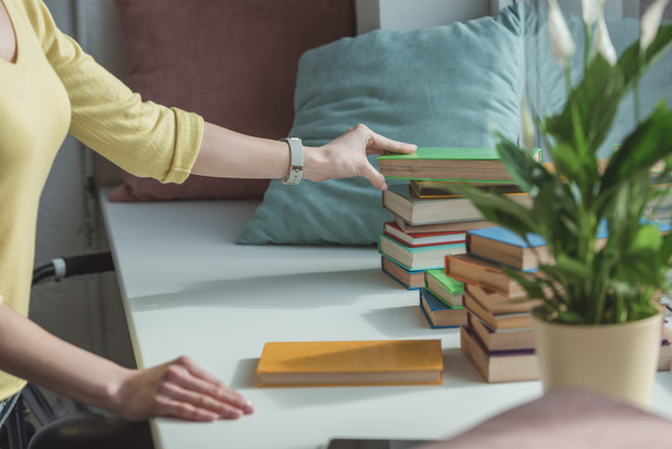 cropped image of woman taking book from stack on windowsill - Foto, Imagen