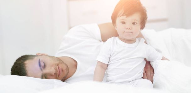 Маленький хлопчик сидить на ліжку вдома зі своїм батьком
 - Фото, зображення