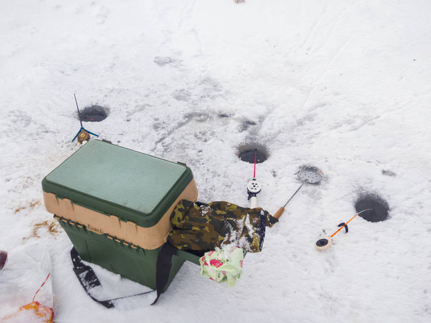 Cañas de pescar de invierno con skimmer y pequeños peces en el hielo cerca de los agujeros de pesca y la suite del pescador en el hielo
 - Foto, Imagen