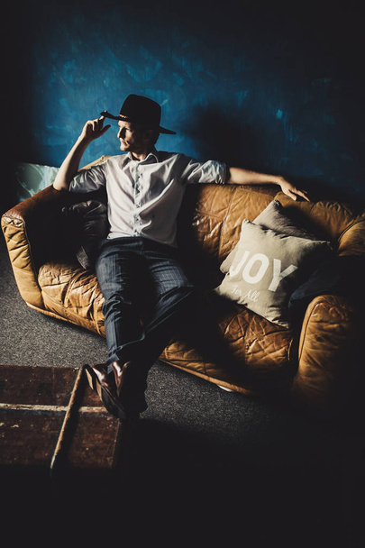 portrait of young handsome man in hat on brown sofa at room background - Fotografie, Obrázek
