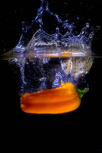 A yellow pepper is dropped into water. - Foto, afbeelding