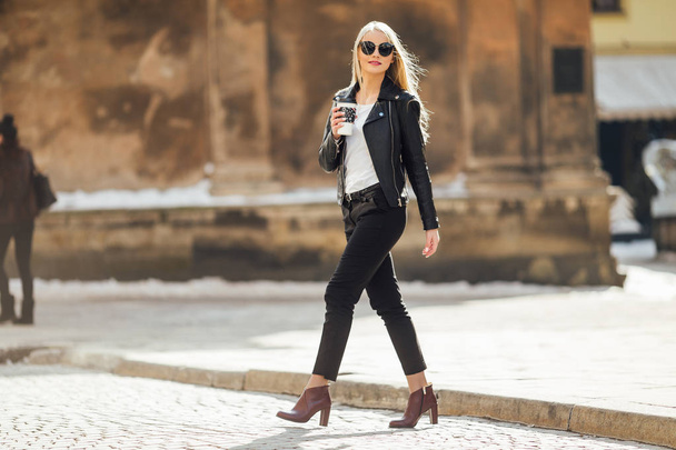 Young pretty girl walk on the street with cup of coffee on her h - Foto, Bild