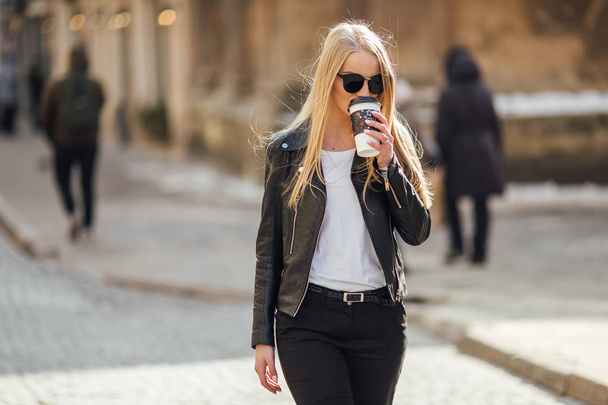 Young pretty girl walk on the street with cup of coffee on her h - Fotoğraf, Görsel