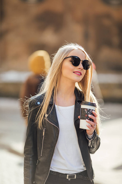Young pretty girl walk on the street with cup of coffee on her h - Фото, зображення