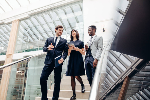 Three multiracial business people walking down on stairs with digital tablet - Foto, immagini
