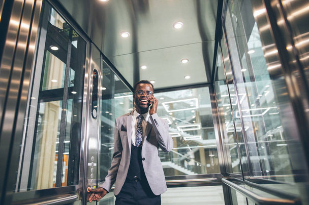 afroamerican businessman in modern glass elevator talking on phone - Foto, afbeelding