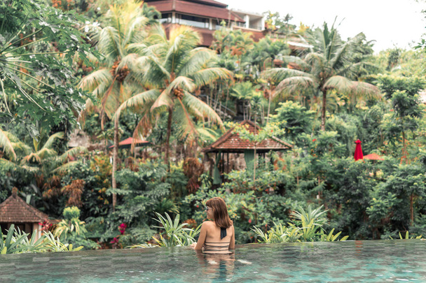 Happy young woman in a tropical infinity pool. Luxury resort on Bali island. - Photo, Image