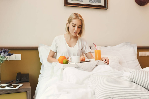 Beautiful young woman sitting on bed and having breakfast - Photo, image