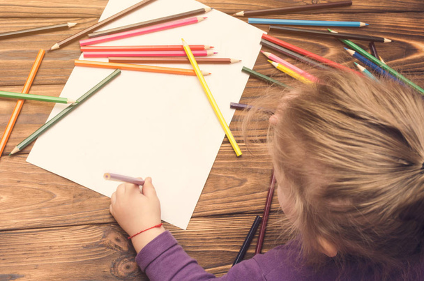 Little girl draws with pencils on a wooden table - Foto, afbeelding